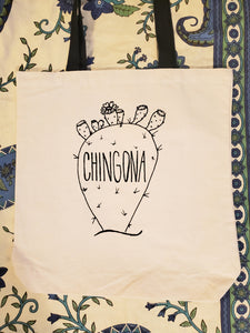 A beige tote bag that has the image of a cactus on it and small blossoms. The words "Chingona" are printed on the cactus.