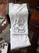 Load image into Gallery viewer, A closeup of our femme support illustrate on a white v-neck t-shirt. They are folded and leaning against a box.
