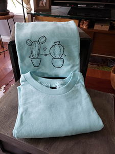 A closeup of our cacti holding hands on a light blue t-shirt. They are folded and leaning against a box.