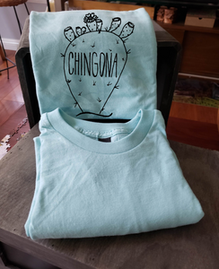 Our sky blue tee with a nopal that reads "chingona". The tee is folded and propped up on a box.