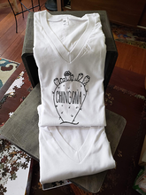Load image into Gallery viewer, Our white v-neck tee with a nopal that reads &quot;chingona&quot;. The tee is folded and propped up on a box.
